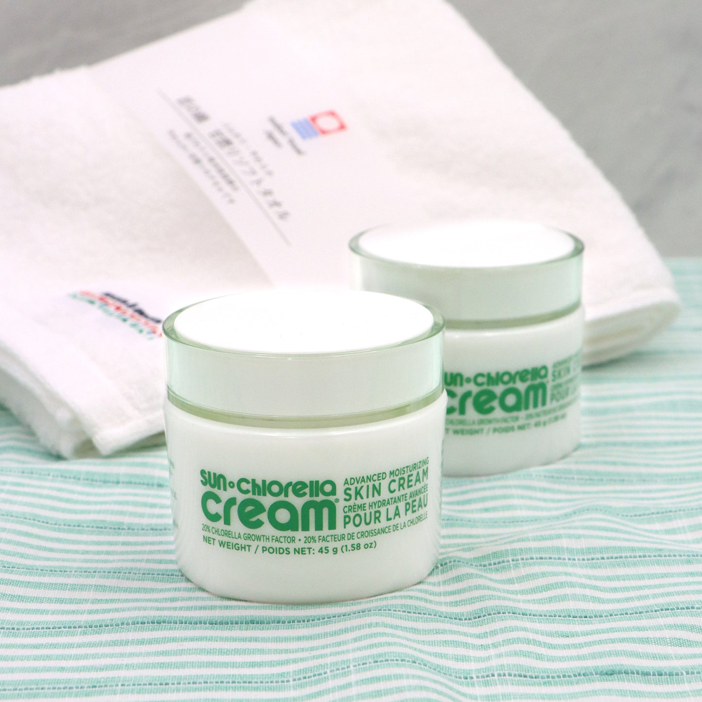 Two jars of Sun Chlorella Cream placed on a striped surface with a complimentary Premium Imabari Face Towel mentioned in the description.