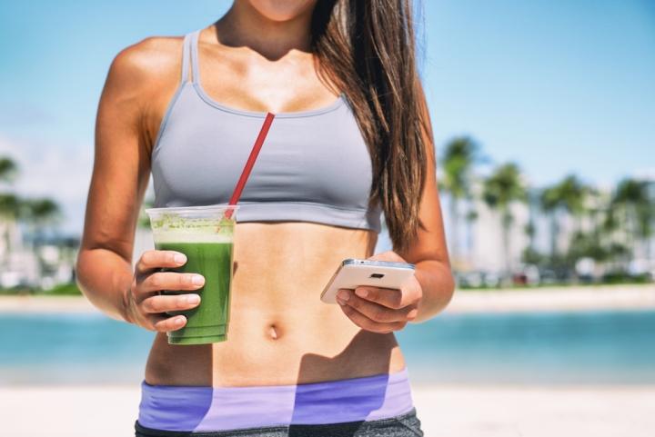 Woman midsection holding green smoothie and mobile phone