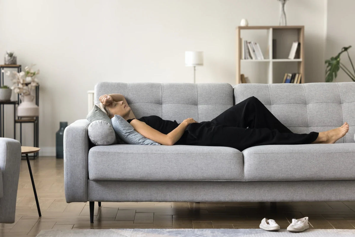 An exhausted woman on a couch, wondering how she can boost her energy in perimenopause.