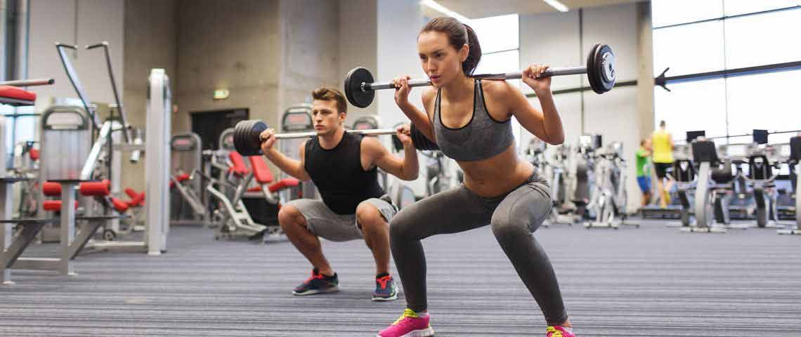 A man and woman both squatting with a barbell