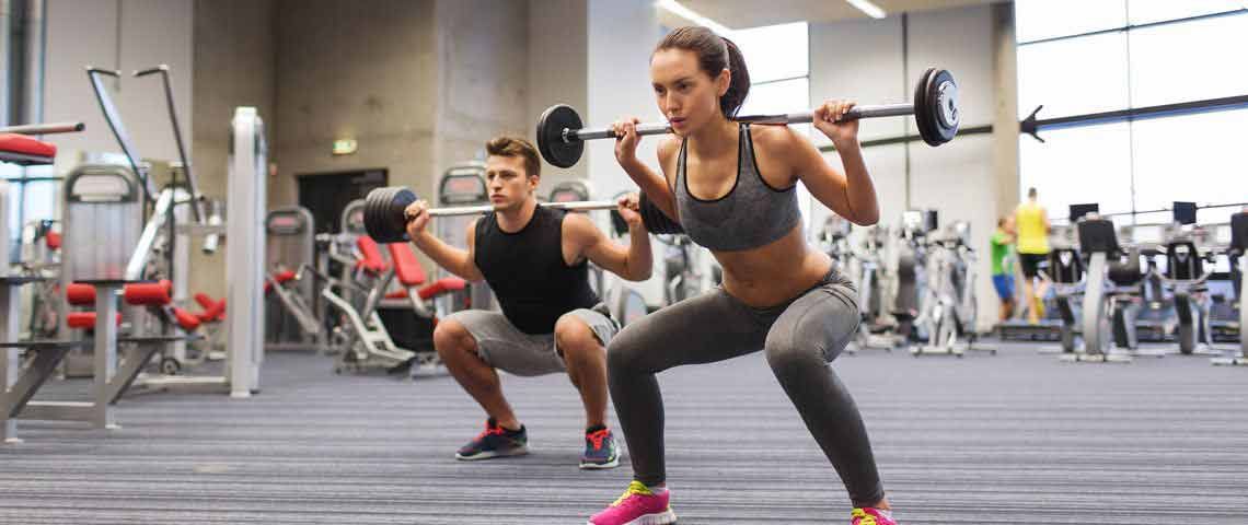 A man and woman both squatting with a barbell A man and woman both squatting with a barbell
