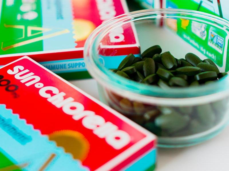 Sun Chlorella powder in a small glass bowl next to packaged Sun Chlorella tablets Sun Chlorella powder in a small glass bowl next to packaged Sun Chlorella tablets