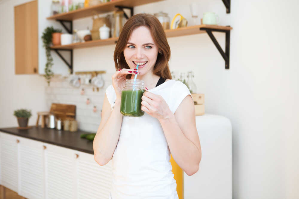 Happy young woman drinking green smoothie