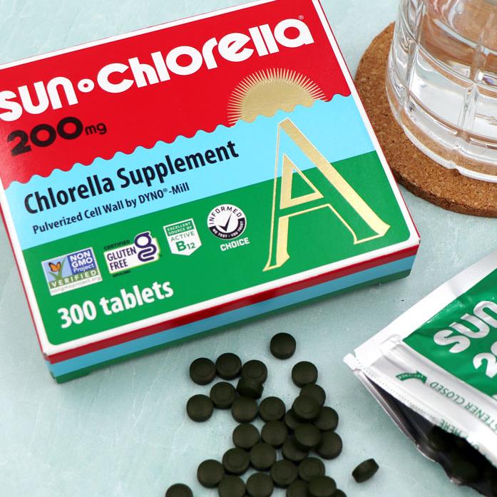 Sun Chlorella 200mg 300 Tablets box on the table next to a water filled glass and opened chlorella tablet pouch