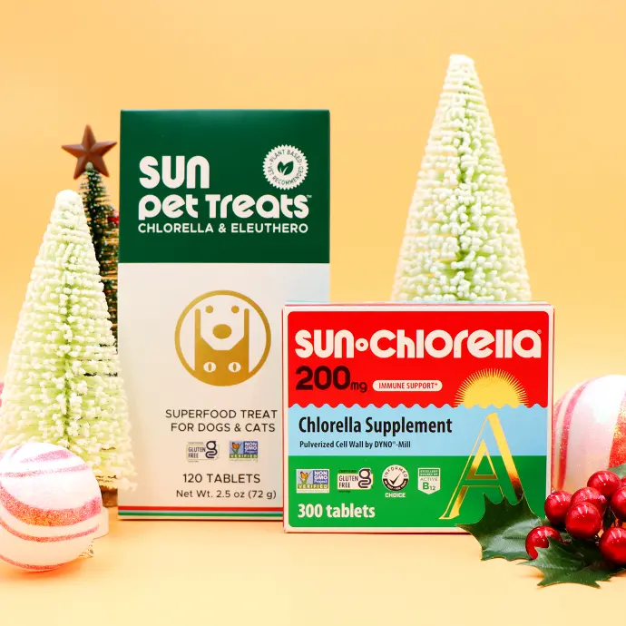 A box of Sun Pet Treats side by side with a box of Sun Chlorella 200mg tablets surrounded by Christmas themed items
